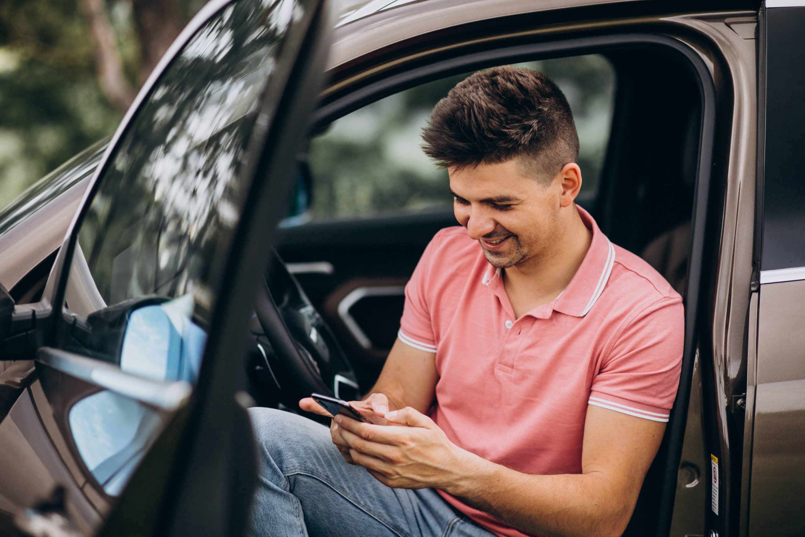 Motorista sentado à porta do carro usando o celular para consultar débitos veiculares e organizar pagamentos com apoio da ConectCar.