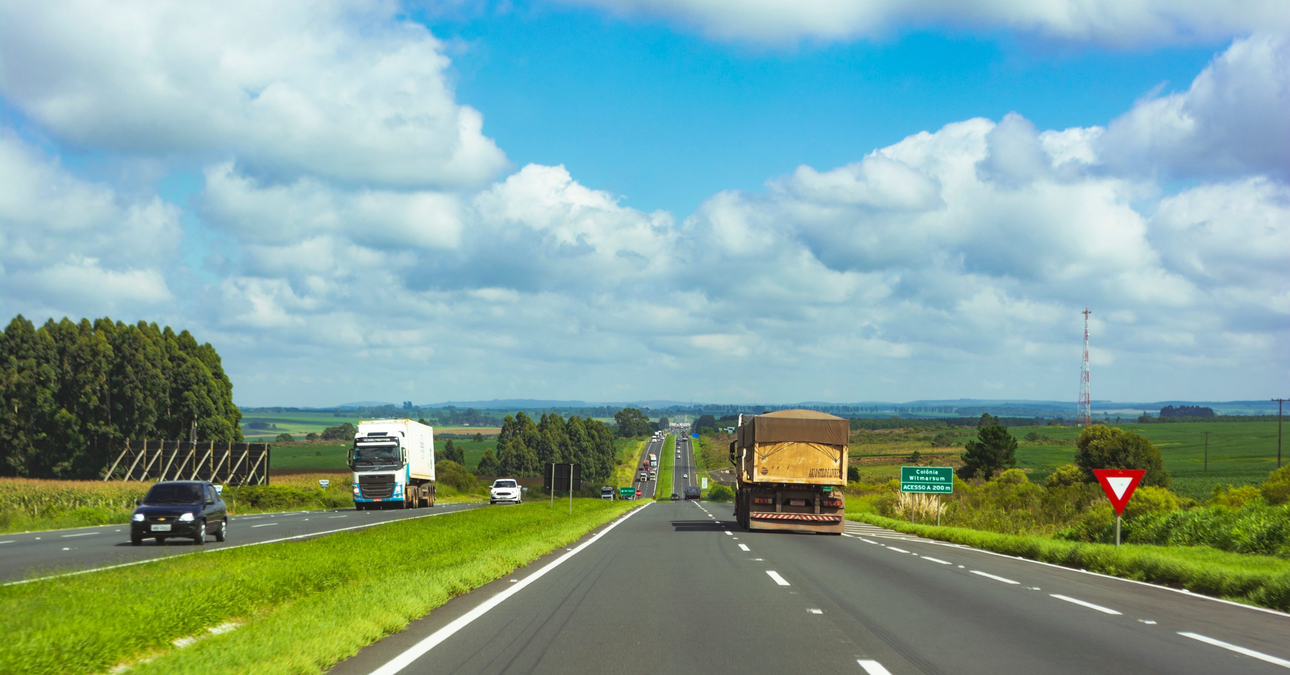 Rodovia no Paraná com tráfego fluindo livremente, caminhões e carros passando por sistema Free Flow, onde a ConectCar permite pagamento automático do pedágio eletrônico.